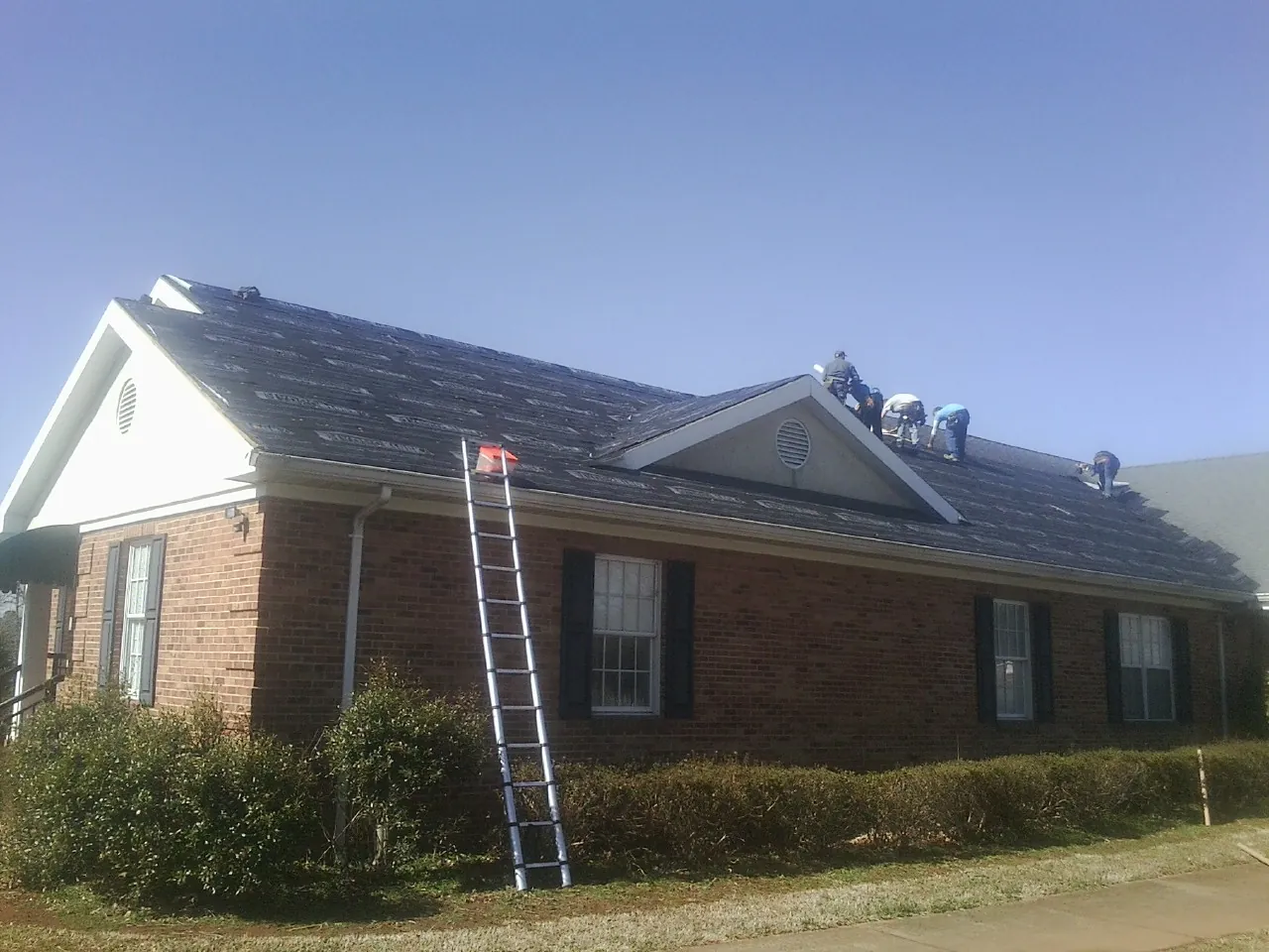 Crew tearing shingles off a brick ranch roof with a ladder set — Metal Roof Repair work by our crew in Garwood