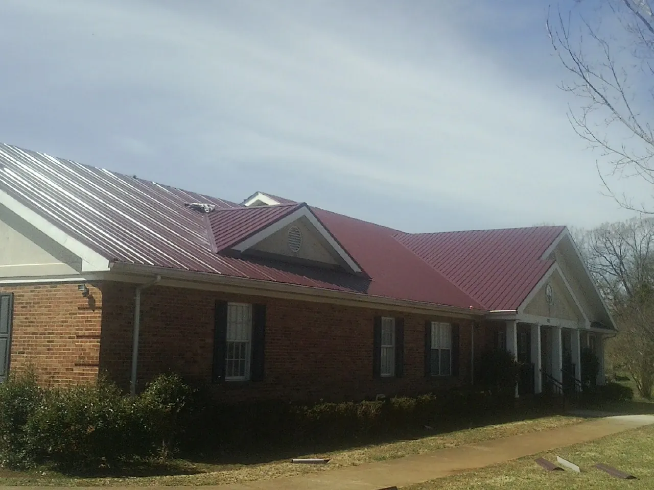 Red metal roof with gabled entries on a long brick building, from a Hail Damage Roof Repair job in Garwood