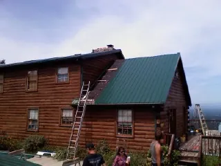 Green metal roof going on a two story log home with ladders set in Garwood