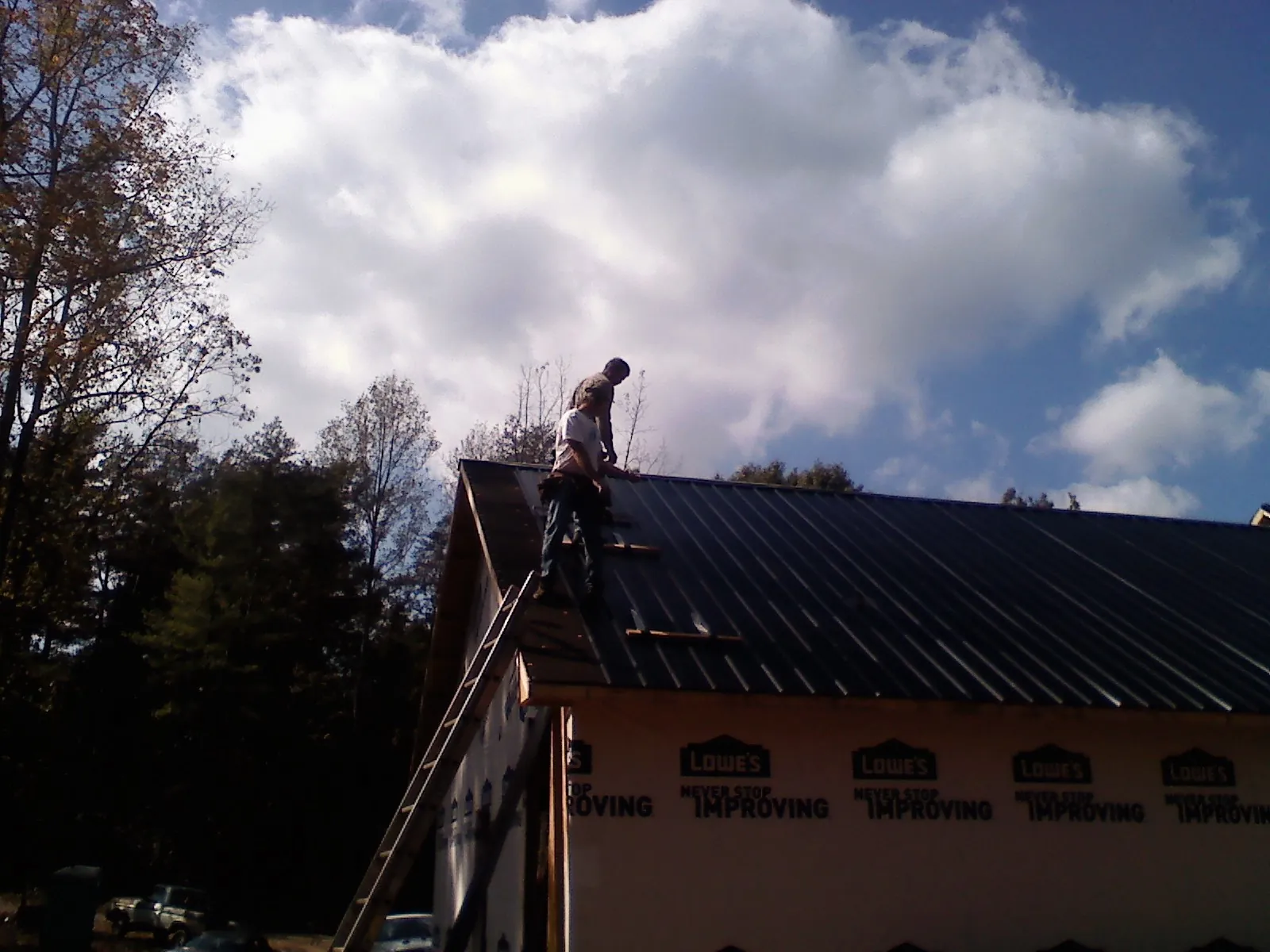 Roofer fastening dark metal panels high against a cloudy sky, from a Roof Inspection job in Garwood